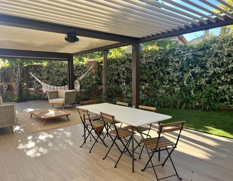 Pérgola de lamas con zona de estar, comedor exterior y hamaca junto a muro de hiedra en bajo en Majadahonda — Abierto al Jardín