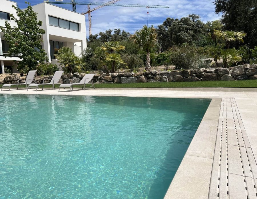 Piscina con canal perimetral y tumbonas junto a muro de piedra en jardín en Madrid — Abierto al Jardín