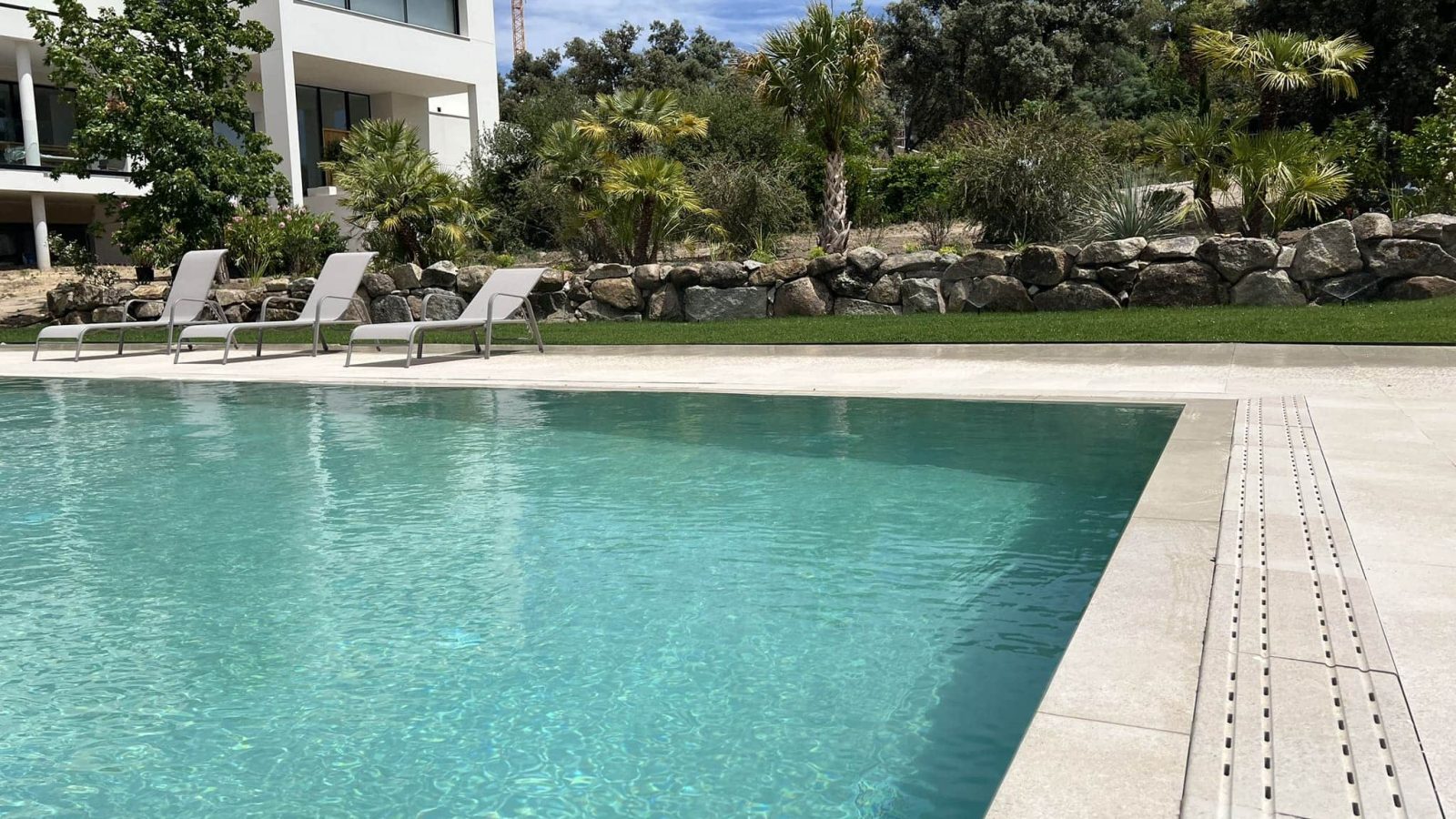 Piscina con canal perimetral y tumbonas junto a muro de piedra en jardín en Madrid — Abierto al Jardín
